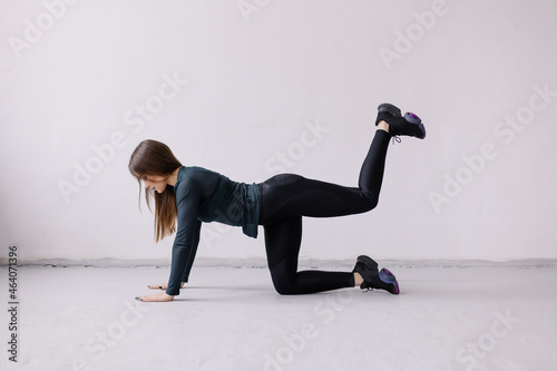 Sporty girl doing exercises in the gym. Leg swing exercise for the buttocks. Black sportswear. Fitness trainer. Healthy lifestyle. Normal muscular body shape. Workout fit. Sport