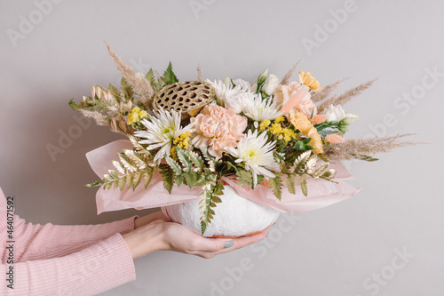 Beautiful autumn flower arrangement in pumpkin on gray background. Woman holds decor for interior