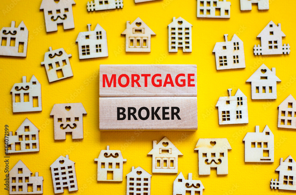 Mortgage broker symbol. Concept words 'Mortgage broker' on wooden blocks near miniature wooden houses. Beautiful yellow background. Business, mortgage broker concept.