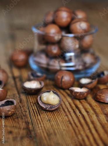 A pile of macadamia nuts in a transparent glass and some others on a wooden surface.
