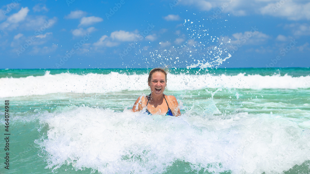 a girl in a bright swimsuit splashes in the blue sea with white waves in sunny weather