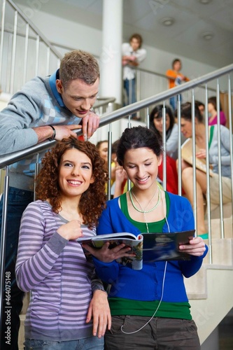 Smiling university students looking at magazine on steps
