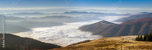 Panorama alpine landscape of the mountain peaks and valleys covered in fog at dawn. Autumn landscape mountains and colorful forest on background sunrise.