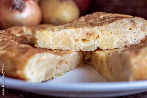 Close-up with selective focus to a Spanish potato omelette with onion, with some ingredients around it.
