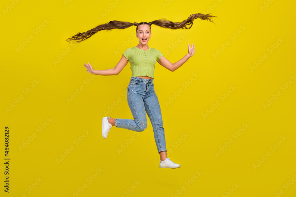 Full length body size view of attractive cheerful girl jumping having fun hair flying isolated over bright yellow color background Full length body size view of attractive cheerful girl jumping having fun hair flying isolated over bright yellow color background