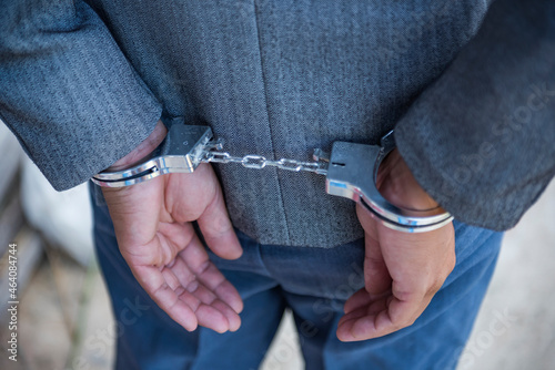 Arrested businessman in handcuffs with hands behind back.