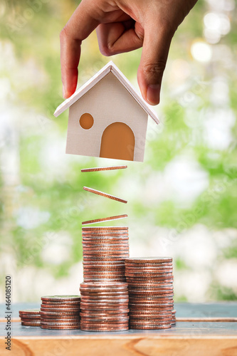 Woman hand hold a home model present to stack gold coin with growing value put on the wood in the public park, Loan or save money for buy real estate to family concept.