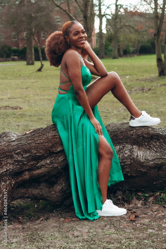 Beautiful African black woman in park in autumn. Beautiful young woman with brown skin. Smiling black woman with afro hair wearing green dress with high slit. Beautiful African black woman in park in autumn. Beautiful young woman with brown skin. Smiling black woman with afro hair wearing green dress with high slit.