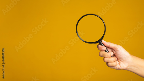 Hand holding a magnifying glass over a yellow background with copy space for text. Close-up photo. Search concept
