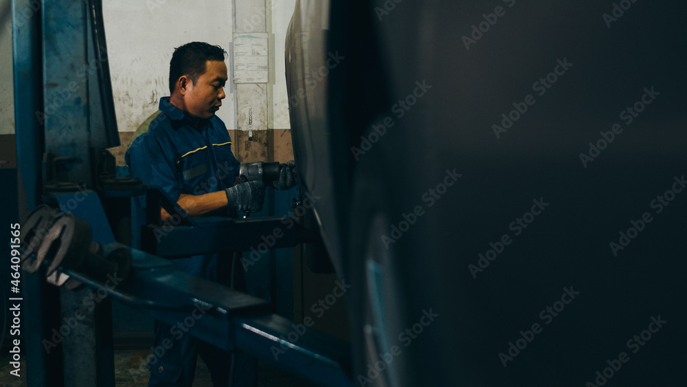 Professional car mechanic changing a car tire on lifted automobile at repair service station. Wheel alignment work at workshop night. Skillful Asian guy in uniform fixing car. Professional car mechanic changing a car tire on lifted automobile at repair service station. Wheel alignment work at workshop night. Skillful Asian guy in uniform fixing car.