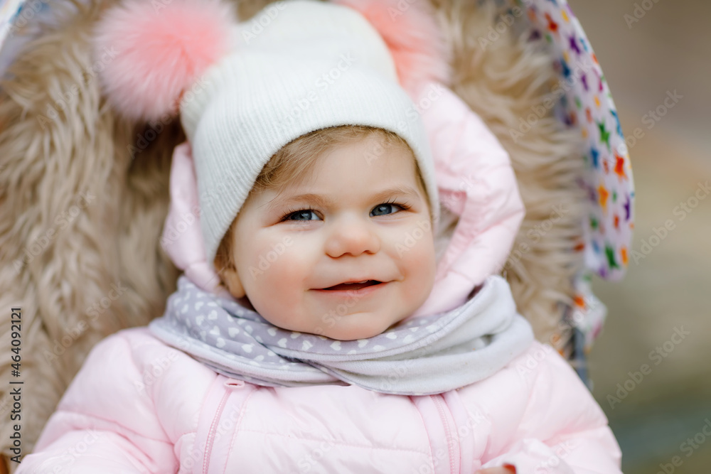 Cute little beautiful baby girl sitting in the pram or stroller on cold autumn, winter or spring day. Happy smiling child in warm clothes, fashion stylish baby coat and hat. Snow falling down Cute little beautiful baby girl sitting in the pram or stroller on cold autumn, winter or spring day. Happy smiling child in warm clothes, fashion stylish baby coat and hat. Snow falling down