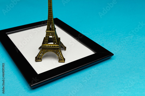 The concept of travel and tourism with a photo frame. The Eiffel Tower stands on a stylish black photo frame with glass on a turquoise background. A place for your photo or text. Side view from above © Evgenii