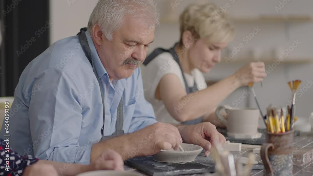 A group of elderly people at a master class in pottery together sculpt and cut a drawing on cups of clay for the manufacture of ceramic dishes A group of elderly people at a master class in pottery together sculpt and cut a drawing on cups of clay for the manufacture of ceramic dishes
