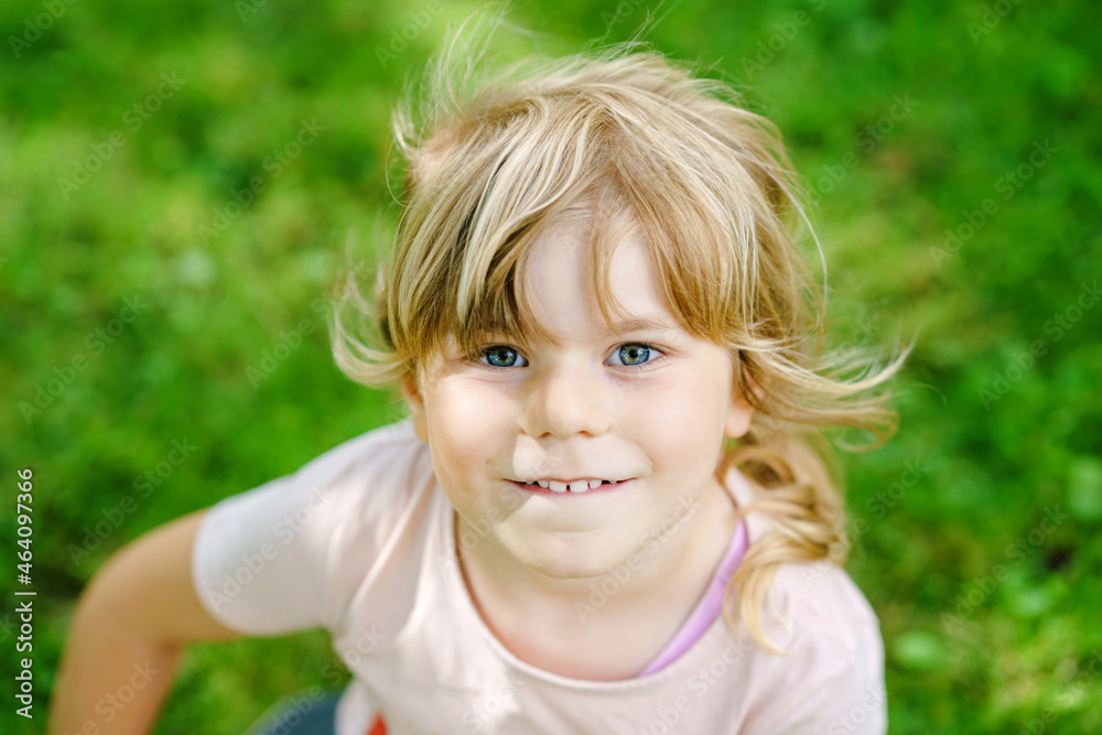 Portrait of happy smiling preschool girl outdoors. Little child with blond hairs looking and smiling at the camera. Happy healthy child enjoy outdoor activity and playing. Portrait of happy smiling preschool girl outdoors. Little child with blond hairs looking and smiling at the camera. Happy healthy child enjoy outdoor activity and playing.
