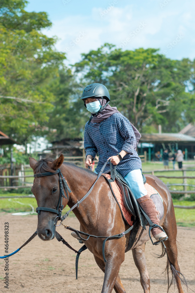 Women with mask and hijab learns to ride a horse. girls riding horses at the ranch. equestrian sport during the pandemic