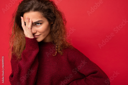 Young attractive curly brunette female person with sincere emotions poising isolated on background wall with copy space wearing casual dark red sweater. wtf concept