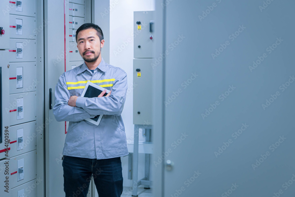 Electrical engineer working check the electric current voltage and overload at front of load center cabinet or consumer unit for maintenance with tablet in main power distribution system room.