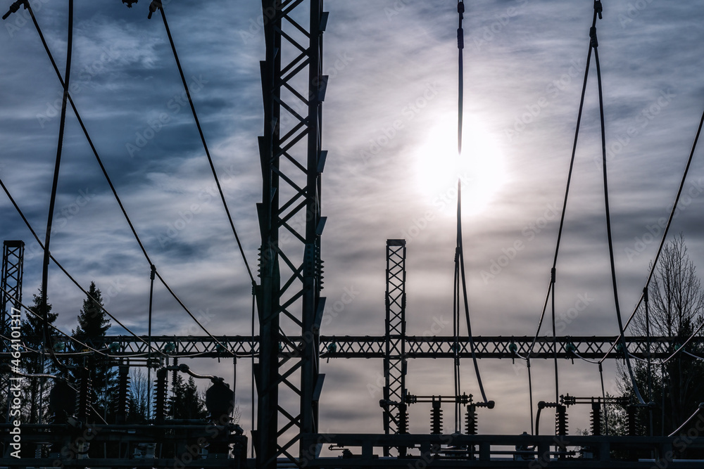 High voltage power transformer substation - wires with Sun at background