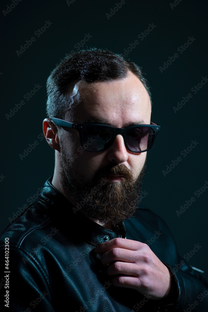 Fototapeta premium dramatic portrait of bearded millennial guy in leather jacket on dark background