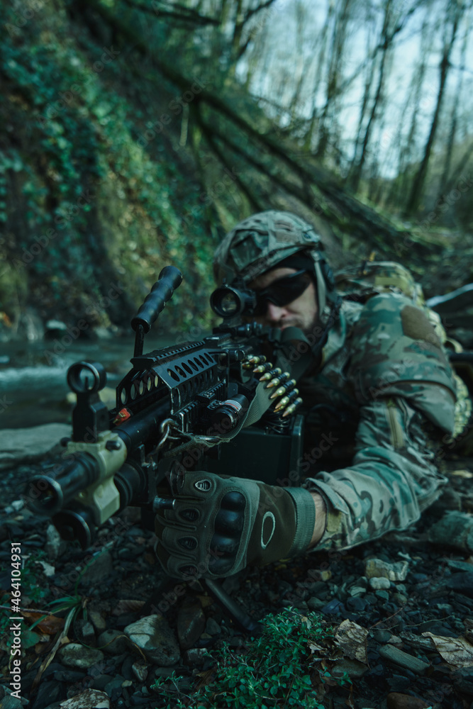 Portrait of airsoft player in professional equipment in helmet aiming at victim with gun in the forest. Soldier with weapons at war