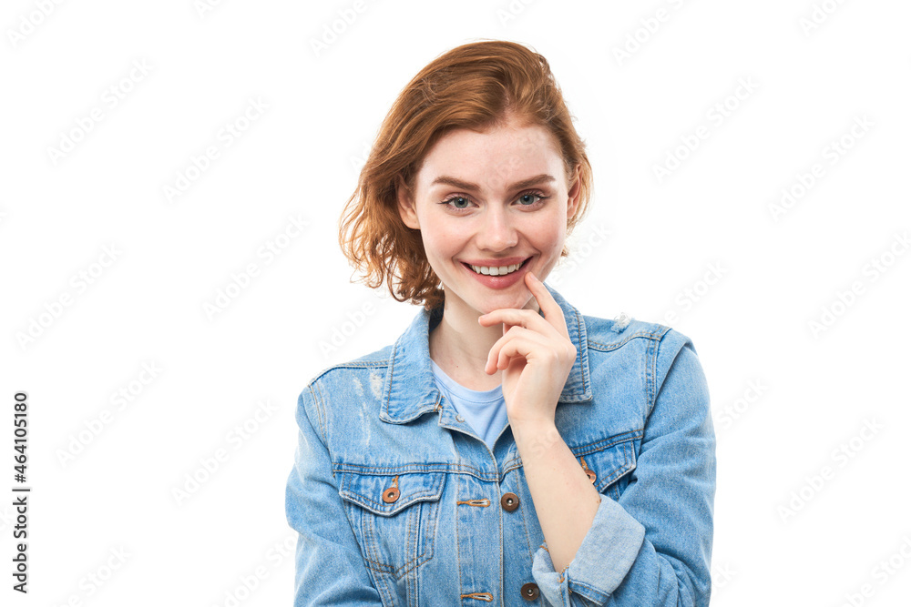 A girl student with red hair happily thinks and looks at the camera while holding her finger near her chin. Pensive thoughtful woman in a blue denim jacket on a white background. Copy space A girl student with red hair happily thinks and looks at the camera while holding her finger near her chin. Pensive thoughtful woman in a blue denim jacket on a white background. Copy space