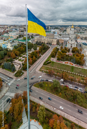 Flagpole with the flag of Ukraine, autumn colorful city aerial vertical panorama view near river Lopan embankment, Skver Strilka, Dormition Cathedral in Kharkiv, Ukraine