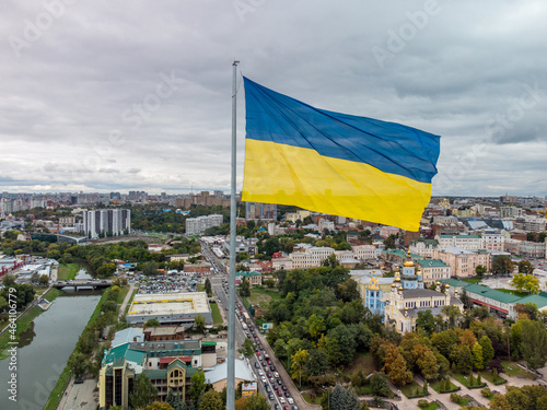 Flag of Ukraine waving close-up with epic gray cloudscape, city aerial view near river Lopan embankment, Svyato-Pokrovskyy Monastyr in Kharkiv, Ukraine