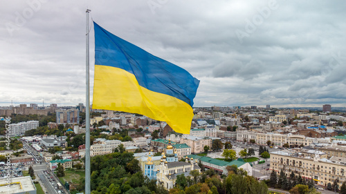 Flag of Ukraine waving with epic gray cloudscape, autumn city aerial view near river Lopan embankment, Svyato-Pokrovskyy Monastyr in Kharkiv, Ukraine photo