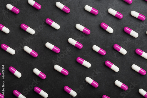 A pattern of pink and white medical pills on a black background