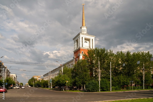 An administrative building with a spire tower is located at the corner of Karl Marx and Robespierre streets on a summer day in the city of Krasnoyarsk, Russia.