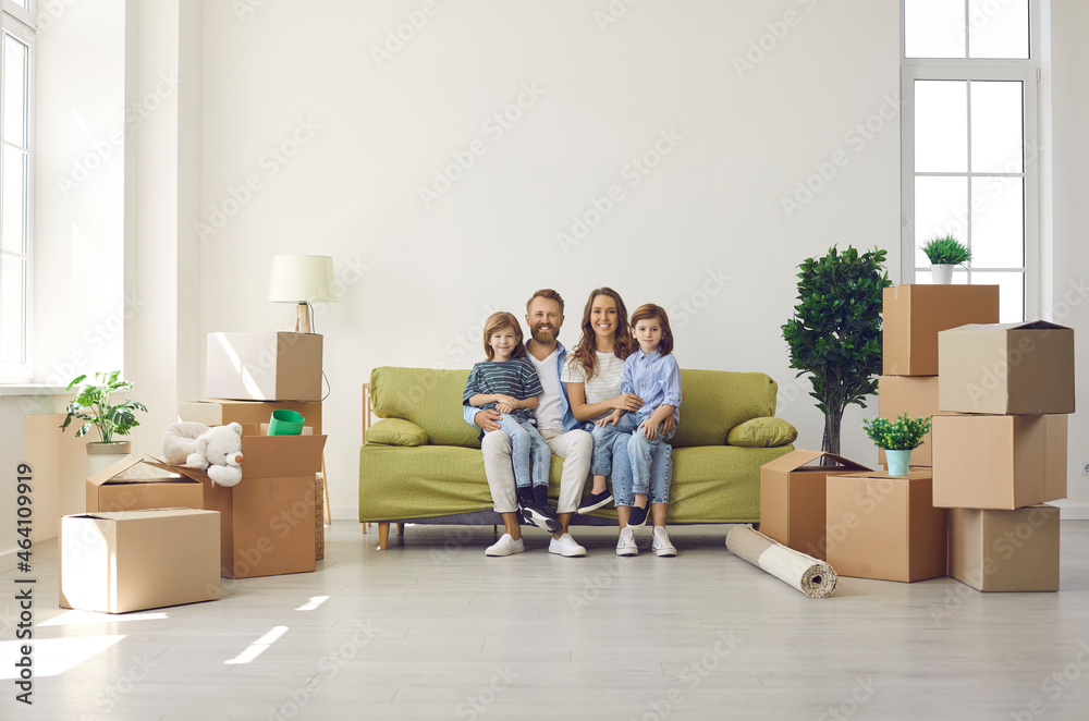Happy family in their new home on moving day. Portrait of mum, dad and kids sitting on sofa in new house or apartment full of unpacked cardboard boxes. Real estate, mortgage, buying property concept Happy family in their new home on moving day. Portrait of mum, dad and kids sitting on sofa in new house or apartment full of unpacked cardboard boxes. Real estate, mortgage, buying property concept