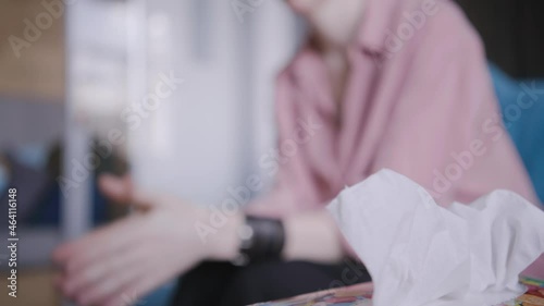 Nervous woman in pink shirt takes and crumples kleenex talking to skilled psychotherapist on comfortable couch in light clinic office close view photo
