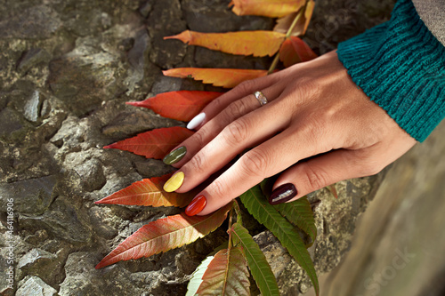 Hands of a beautiful woman on autumn leaves background. Delicate hands with colorful manicure touching leaves. Multicolored nails in fall colors.
