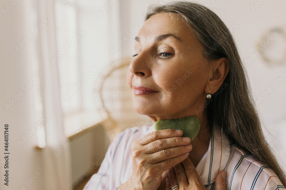 Pretty elderly lady using gua sha for making facial massage helping relieve  tension in face, reduce puffiness and inflammation, working on neck area.  Body care, beauty, aging gracefully Photos | Adobe Stock