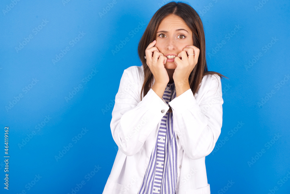Fearful young european doctor girl wearing white medical gown on white background keeps hands near mouth, feels frightened and scared, has a phobia, Shock and frighted concept. Fearful young european doctor girl wearing white medical gown on white background keeps hands near mouth, feels frightened and scared, has a phobia, Shock and frighted concept.