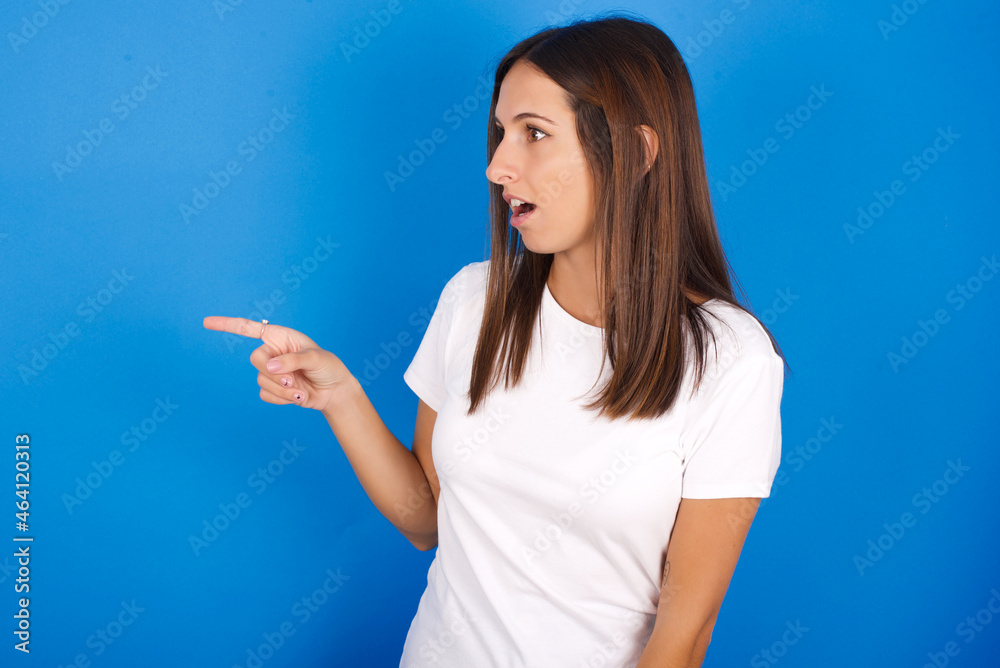 Stunned young european girl wearing white t-shirt on white background with greatly surprised expression points away on copy space, indicates something Stunned young european girl wearing white t-shirt on white background with greatly surprised expression points away on copy space, indicates something