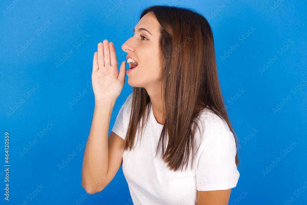young european girl wearing white t-shirt on white background look empty space holding hand near her face and screaming or calling someone. young european girl wearing white t-shirt on white background look empty space holding hand near her face and screaming or calling someone.