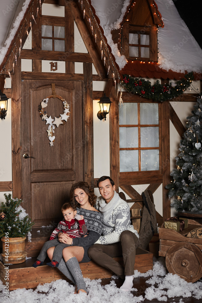 Young beautiful woman, her handsome husband and their cute little son posing on the stairs of decorated for Christmas house