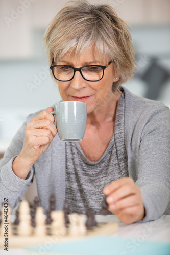 an old woman is playing chess holding a mug