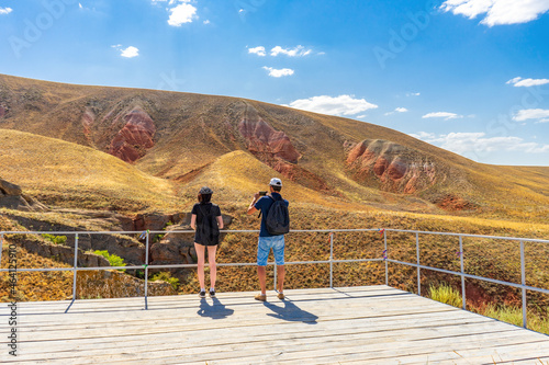 Family couple travelers walking in mountain area. Rear view of man and woman standing on trail against Martian landscapes of red hills. Bogdo Baskunchak Nature Reserve, Astrakhan region, Russia photo
