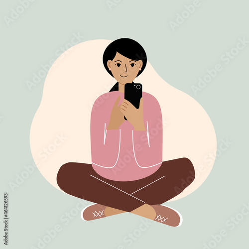 Joyful woman with mobile phone, front view. Taking pictures, reading, chatting. The woman is sitting cross-legged.