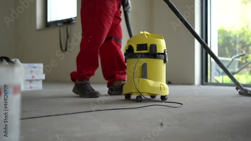 Mature gray-bearded construction worker in overalls vacuums a newly built home. Real estate and interior decoration concept. Real estate construction, country cottages