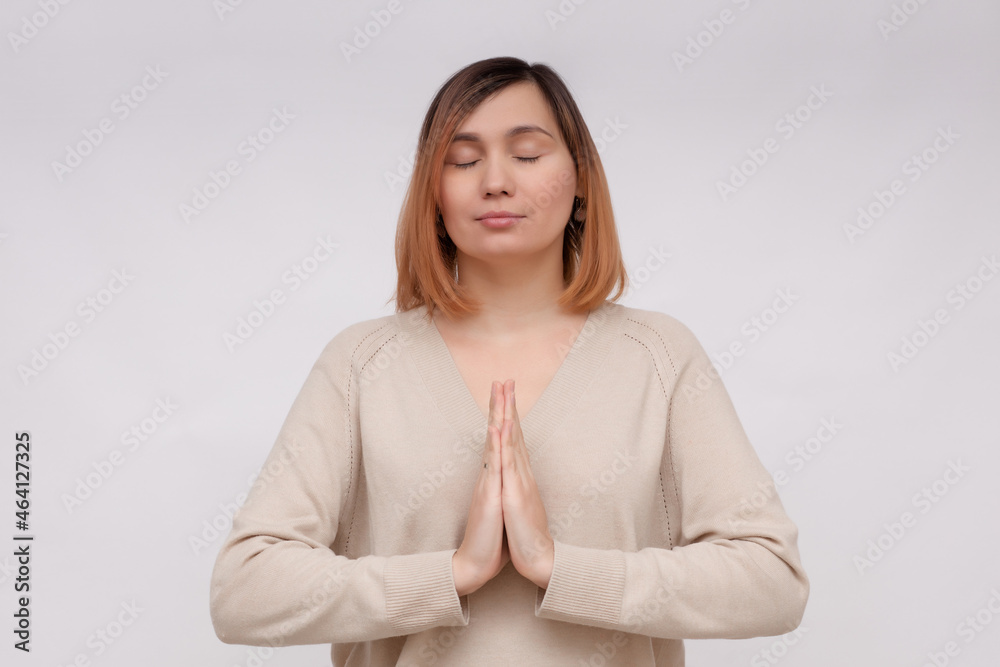 Calm young woman meditating, show namaste pray gesture, close eyes and smiling, making wish, pleading god, standing over white background Calm young woman meditating, show namaste pray gesture, close eyes and smiling, making wish, pleading god, standing over white background