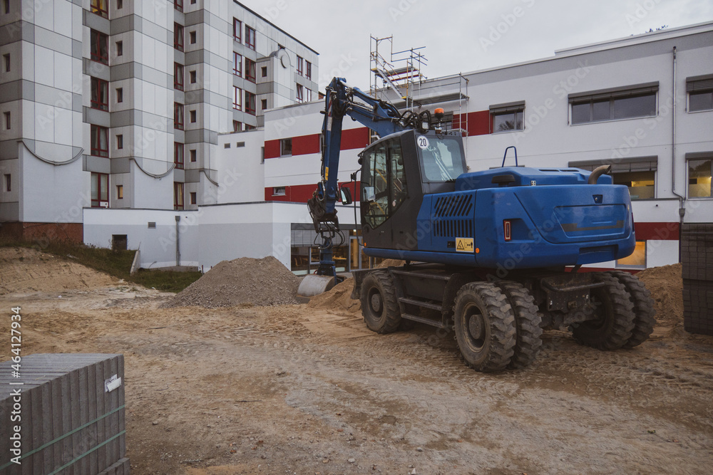  excavator stands on a construction site in front of a white building