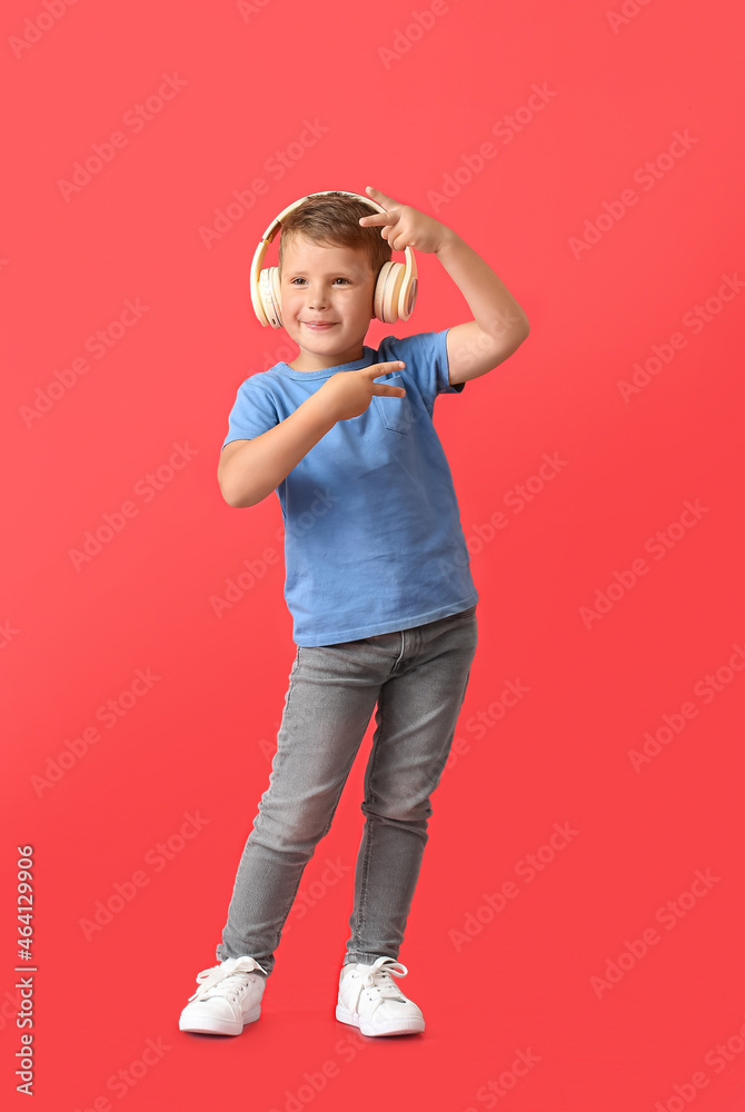 Cute little boy in wireless headphones dancing on red background