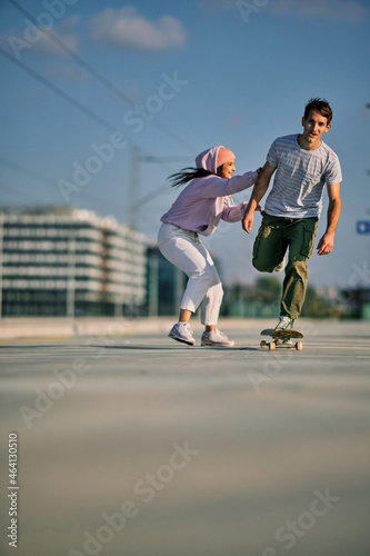 Playful teenagers playing games. A boy riding a skateboard while a girl pushing him.