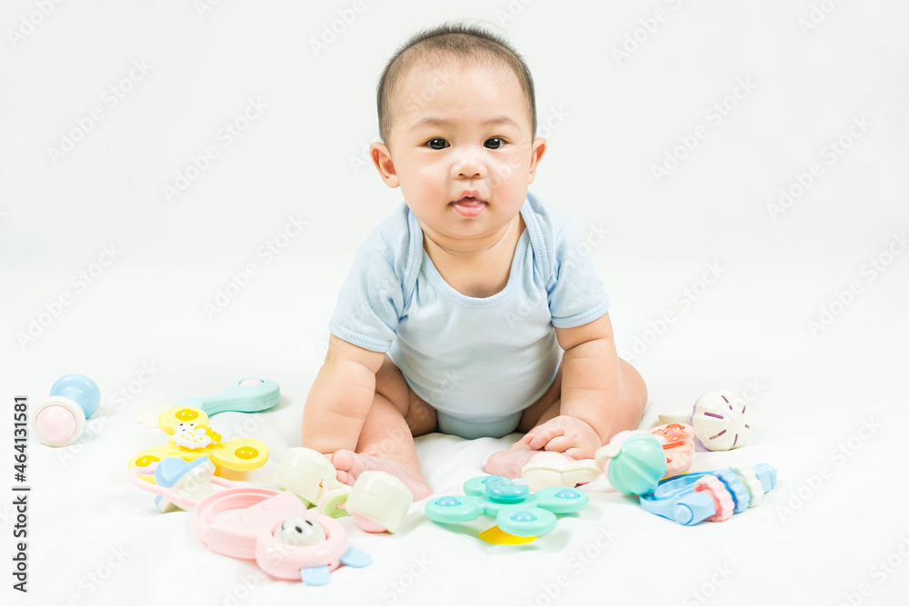 childhood and Childcare concept Portrait of cute little 5 months old  asian newborn baby boy wearing blue bodysuit sitting with colorful development toys on white blanket at home