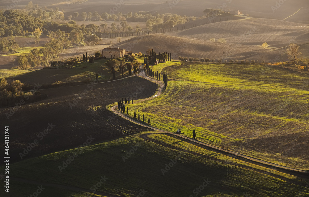 Early morning beautiful Tuscany hills landscape view with plowed and green grass covered wavy fields. Sunrise light covers the meadows and fields making magic light-shadows playing.