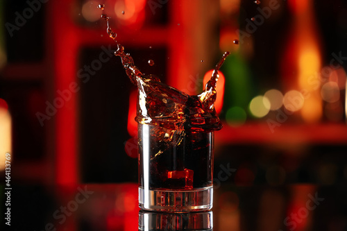 Glass of Cuba Libre cocktail with splash on table against blurred background photo