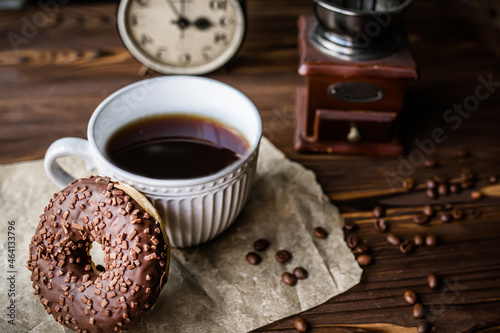 glass of coffee on table with clock in morning. vintage alarm clock showing 9am on the table next to a cup of coffee and a doughnut. Breakfast. Time management concept photo